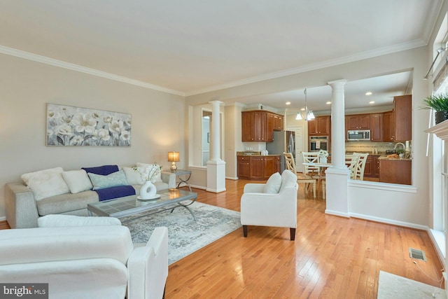 living room featuring visible vents, crown molding, light wood-type flooring, and decorative columns