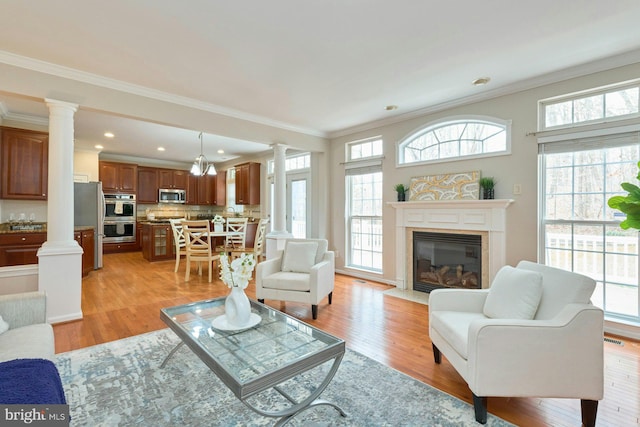 living room with plenty of natural light, light wood-type flooring, and ornate columns