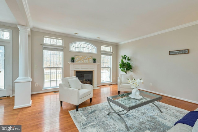 living area with baseboards, light wood-type flooring, ornate columns, and ornamental molding