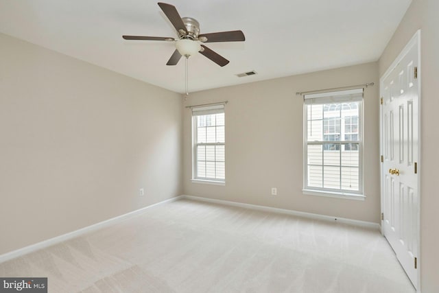 unfurnished room with light carpet, visible vents, a ceiling fan, and baseboards