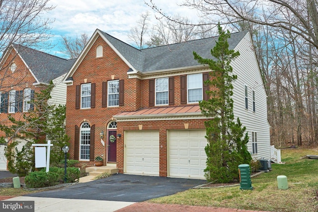 view of front of property with a standing seam roof, aphalt driveway, central AC, a garage, and brick siding