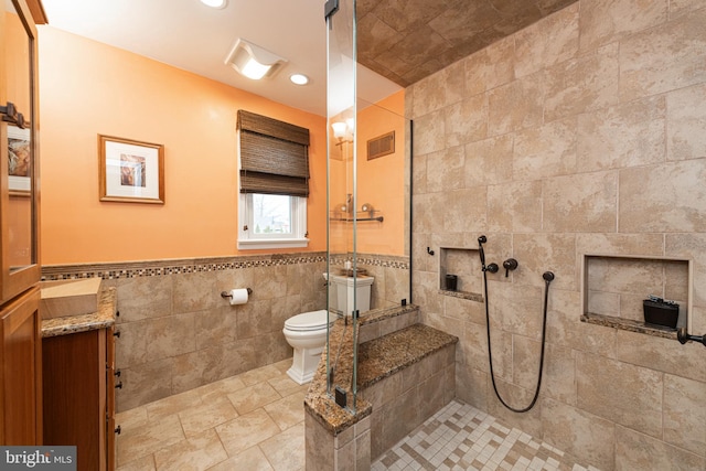 bathroom with vanity, tiled shower, tile walls, and toilet