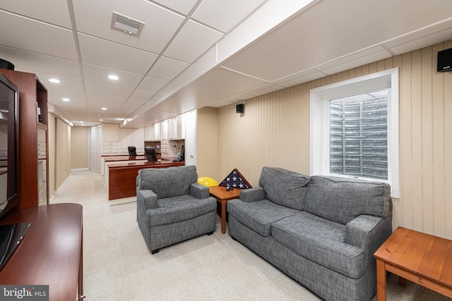 carpeted living room with a drop ceiling and wooden walls