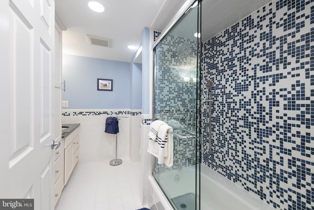 bathroom featuring vanity, combined bath / shower with glass door, tile walls, and tile patterned floors