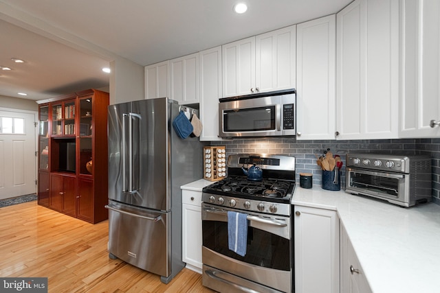 kitchen with stainless steel appliances, white cabinetry, light hardwood / wood-style floors, and decorative backsplash