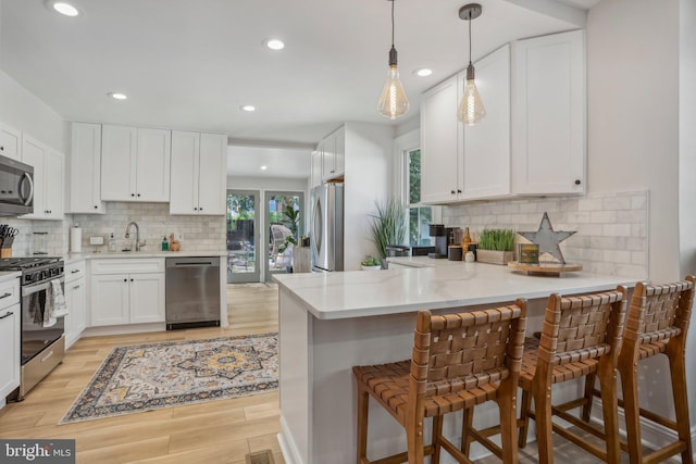 kitchen with white cabinetry, appliances with stainless steel finishes, a kitchen breakfast bar, kitchen peninsula, and pendant lighting