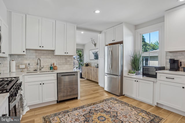 kitchen with stainless steel appliances, white cabinetry, sink, and light hardwood / wood-style floors