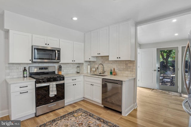 kitchen featuring sink, white cabinets, stainless steel appliances, light hardwood / wood-style floors, and backsplash