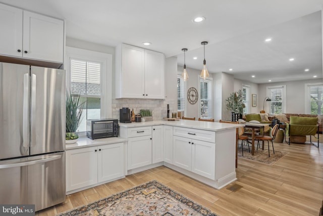 kitchen featuring white cabinetry, decorative light fixtures, stainless steel refrigerator, kitchen peninsula, and light hardwood / wood-style floors