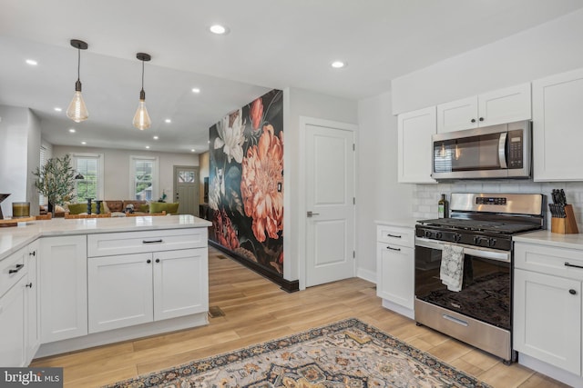 kitchen with white cabinetry, hanging light fixtures, light hardwood / wood-style flooring, and appliances with stainless steel finishes