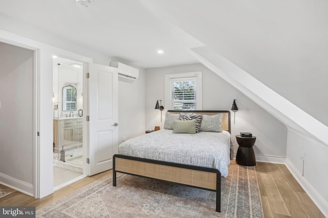 bedroom featuring connected bathroom, hardwood / wood-style flooring, vaulted ceiling, and an AC wall unit