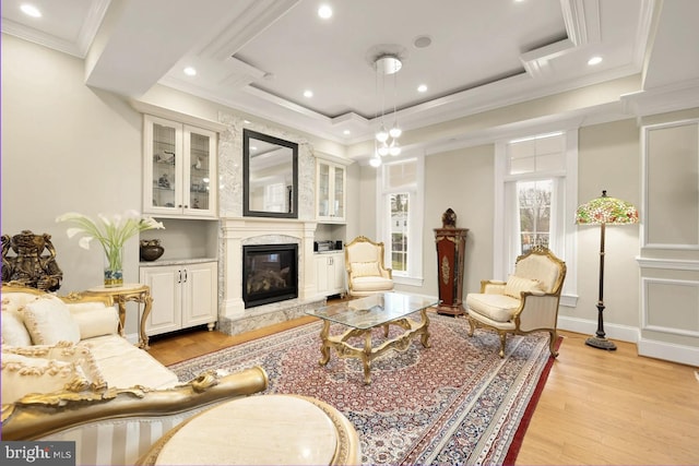 living room with crown molding, a fireplace, light hardwood / wood-style floors, and a raised ceiling