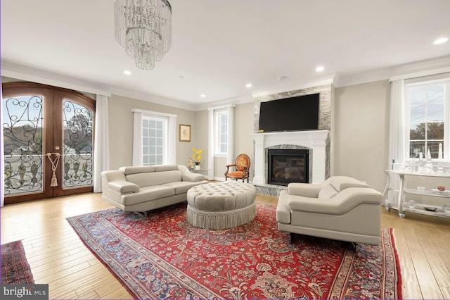 living room with french doors, ornamental molding, a notable chandelier, a high end fireplace, and light hardwood / wood-style flooring