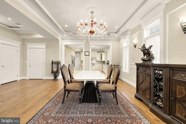 dining space with an inviting chandelier, light hardwood / wood-style flooring, ornamental molding, and a raised ceiling