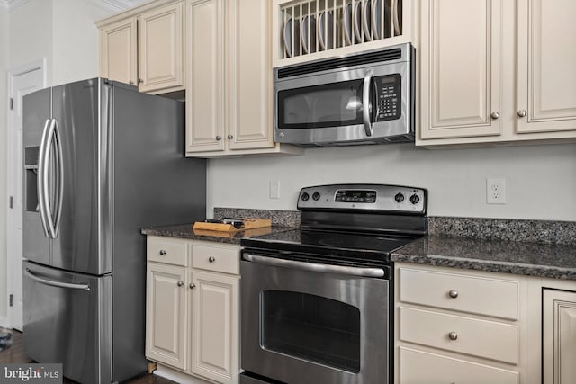 kitchen featuring dark stone countertops, stainless steel appliances, and cream cabinetry