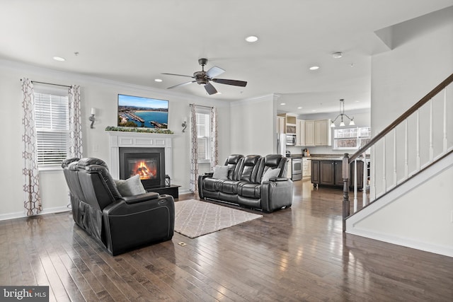 living area featuring dark wood-type flooring, baseboards, stairway, ornamental molding, and a glass covered fireplace