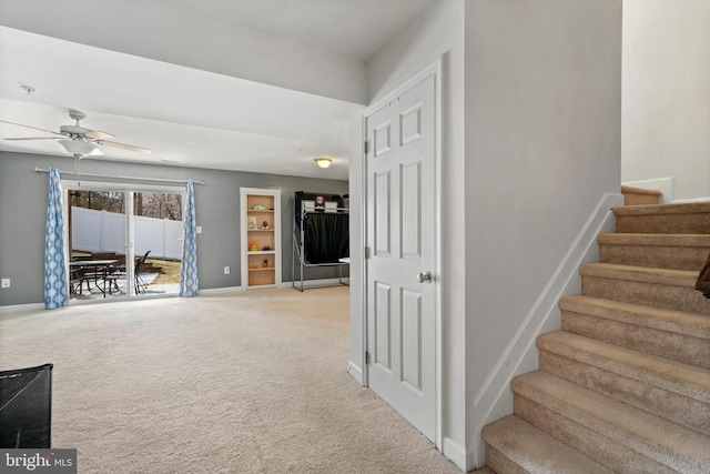 interior space with stairway, light colored carpet, baseboards, and ceiling fan