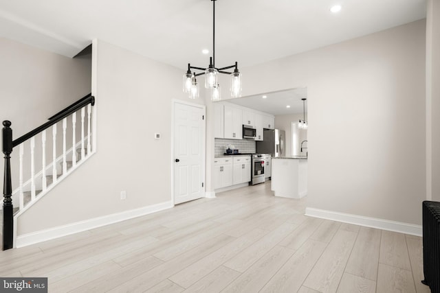 unfurnished living room featuring sink, a chandelier, and light wood-type flooring