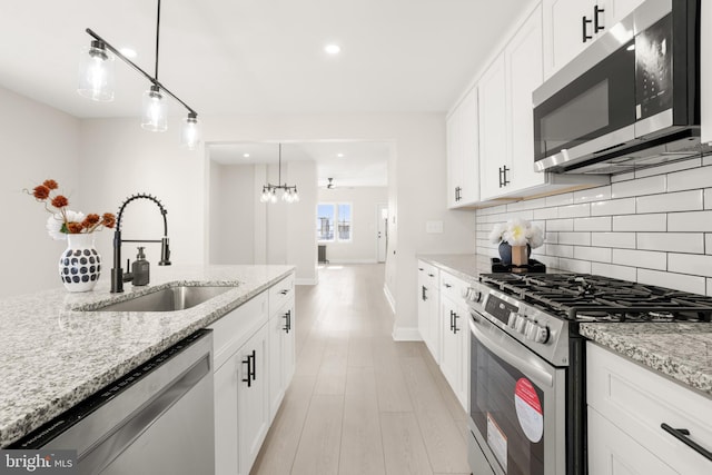 kitchen with white cabinetry, stainless steel appliances, sink, and light stone counters