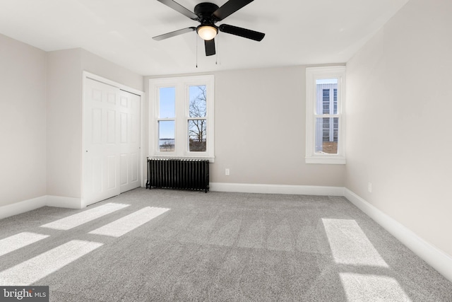 unfurnished bedroom with light carpet, radiator heating unit, ceiling fan, and a closet