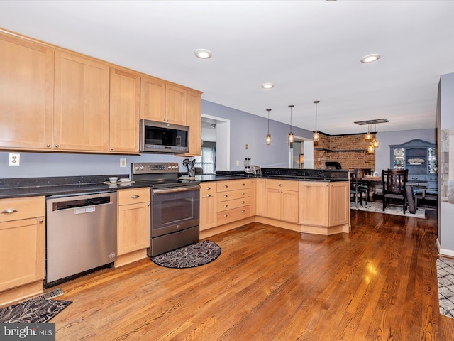 kitchen featuring appliances with stainless steel finishes, hanging light fixtures, hardwood / wood-style flooring, kitchen peninsula, and light brown cabinets