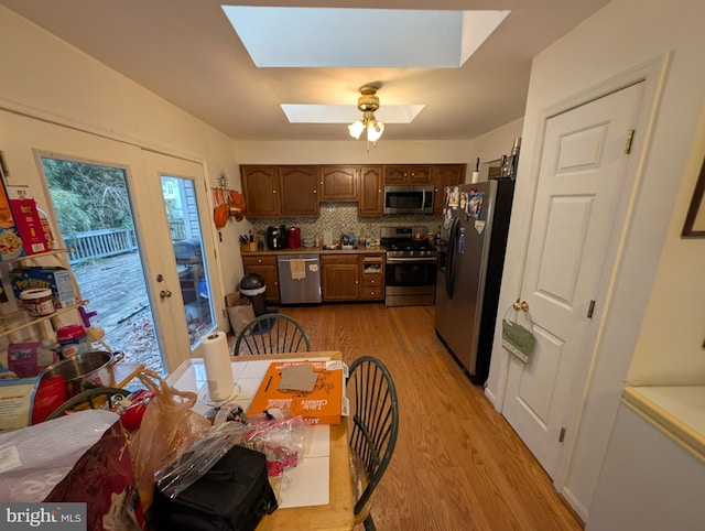 kitchen with light hardwood / wood-style flooring, ceiling fan, a skylight, stainless steel appliances, and tasteful backsplash