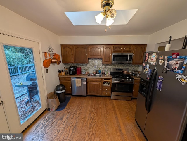 kitchen featuring a skylight, sink, backsplash, stainless steel appliances, and light wood-type flooring