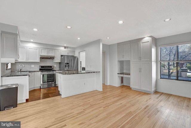 kitchen with appliances with stainless steel finishes, tasteful backsplash, dark stone countertops, white cabinets, and light hardwood / wood-style floors