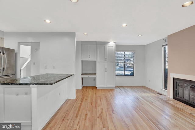 kitchen with white cabinetry, stainless steel refrigerator, dark stone counters, and light wood-type flooring