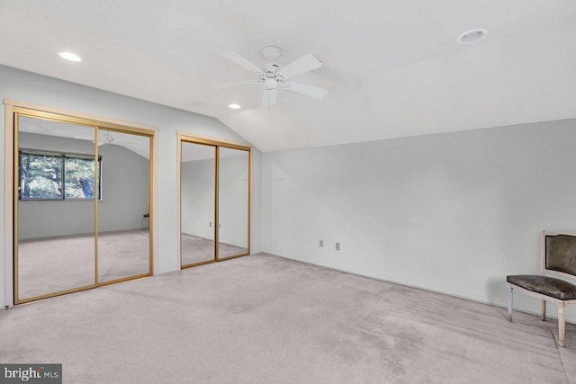 unfurnished bedroom with multiple closets, lofted ceiling, light carpet, and ceiling fan