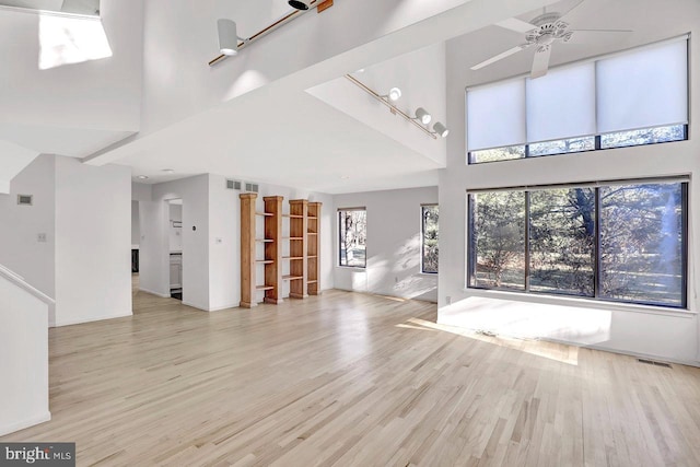 unfurnished living room featuring a towering ceiling, ceiling fan, and light wood-type flooring