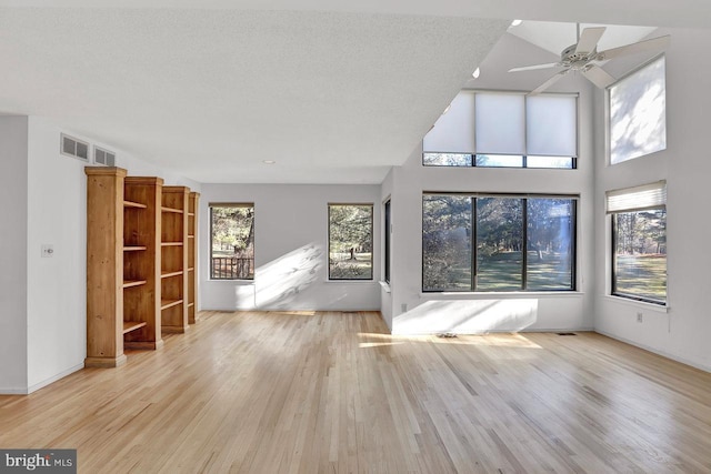 unfurnished living room featuring ceiling fan, a wealth of natural light, light hardwood / wood-style floors, and a textured ceiling