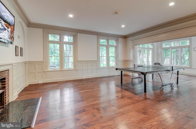 game room with a brick fireplace, crown molding, and dark wood-type flooring