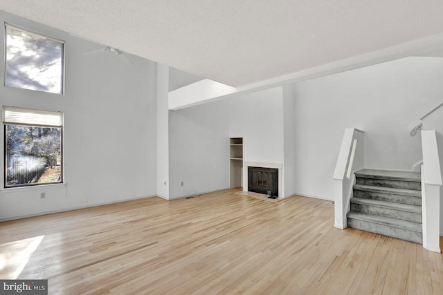 unfurnished living room featuring high vaulted ceiling, a textured ceiling, and light wood-type flooring