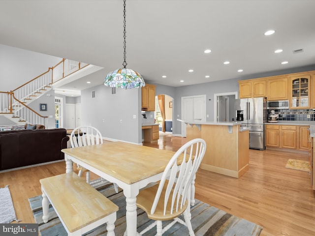 dining area with arched walkways, recessed lighting, light wood finished floors, and stairs