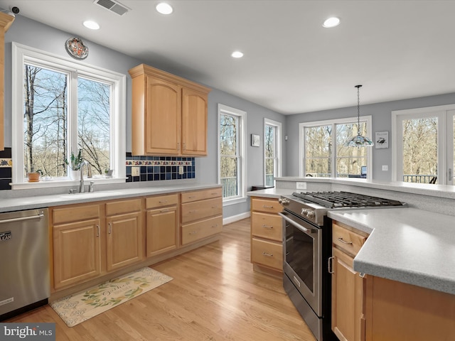 kitchen featuring stainless steel appliances, light countertops, hanging light fixtures, visible vents, and a sink