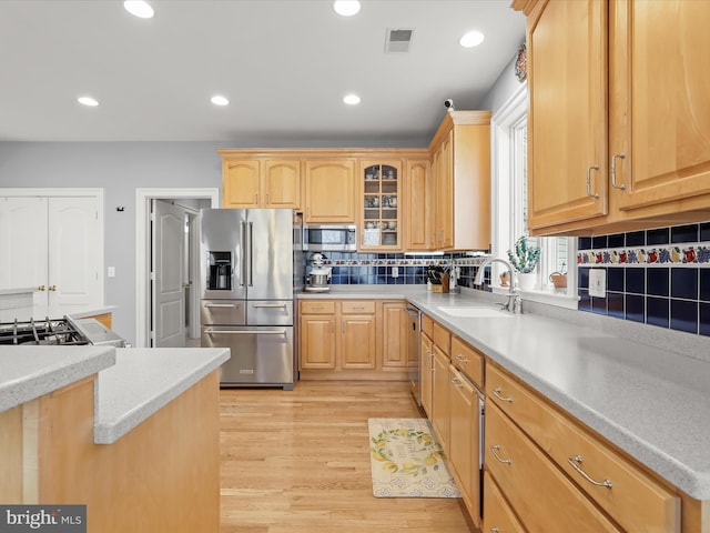 kitchen with light countertops, appliances with stainless steel finishes, a sink, and glass insert cabinets