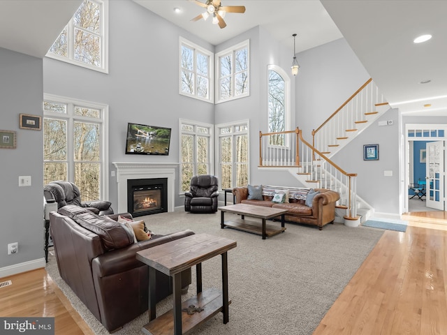 living area featuring stairs, light wood-type flooring, a glass covered fireplace, and baseboards