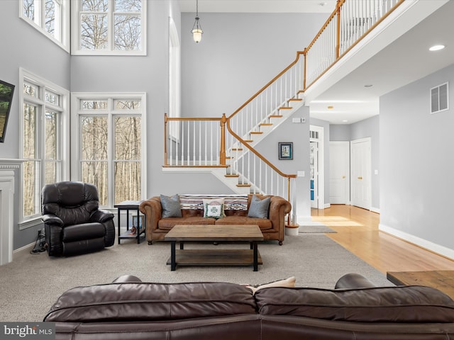 living area with light wood finished floors, visible vents, a high ceiling, baseboards, and stairs