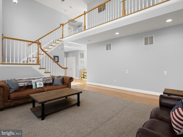 living room with baseboards, visible vents, a towering ceiling, wood finished floors, and stairs