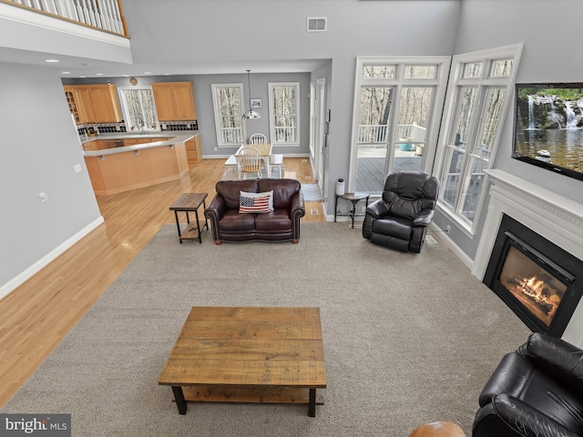 living room with a glass covered fireplace, visible vents, plenty of natural light, and light wood finished floors