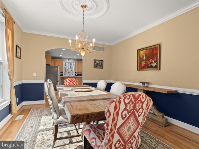 dining room with light wood-type flooring, arched walkways, visible vents, and crown molding