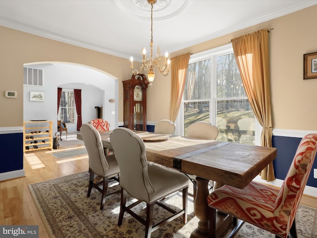 dining space featuring arched walkways, crown molding, a notable chandelier, and light wood-style floors