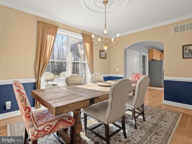 dining space featuring visible vents, arched walkways, baseboards, light wood-style flooring, and ornamental molding