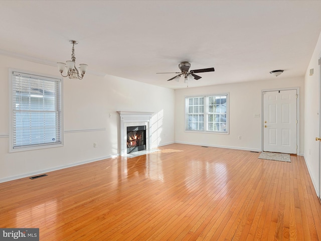 unfurnished living room with ceiling fan with notable chandelier, a high end fireplace, and light hardwood / wood-style flooring