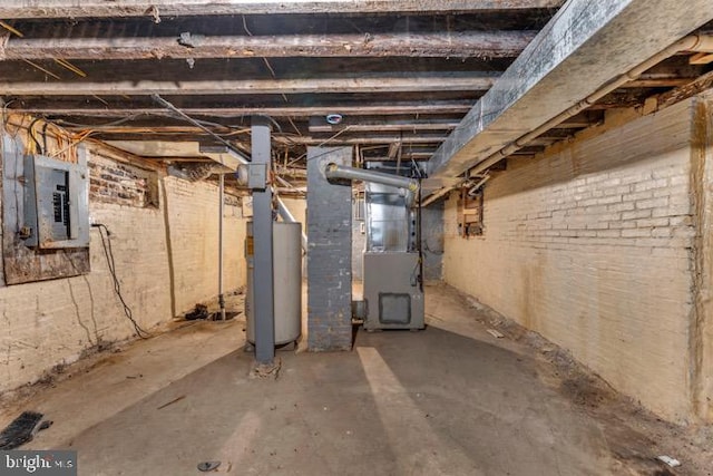 basement featuring heating unit, electric panel, water heater, and brick wall