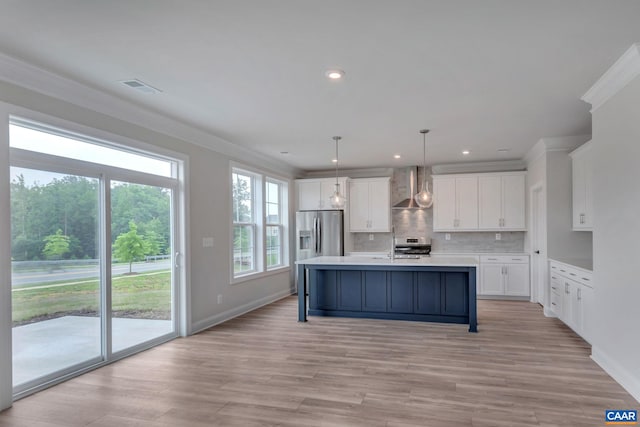 kitchen with wall chimney exhaust hood, appliances with stainless steel finishes, ornamental molding, an island with sink, and pendant lighting