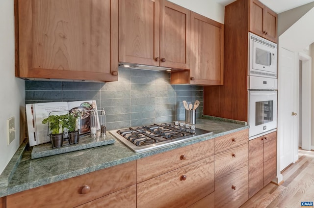 kitchen with light hardwood / wood-style flooring, white appliances, and decorative backsplash