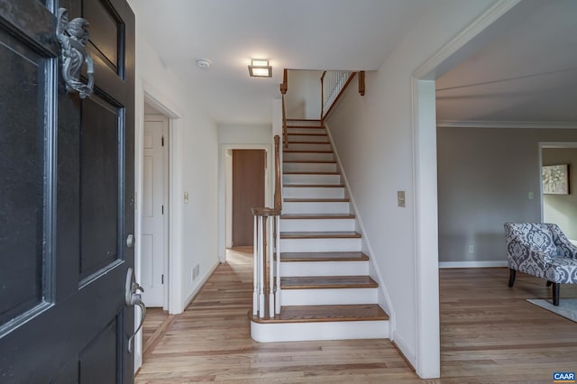 entryway with ornamental molding and light hardwood / wood-style floors