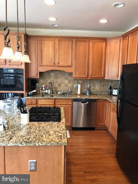 kitchen featuring tasteful backsplash, sink, hanging light fixtures, light stone counters, and black appliances